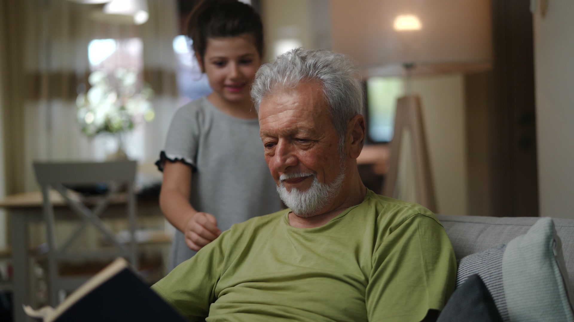 An older man smiles as a child embraces him while he holds an open book.